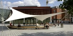 people are sitting on benches in front of a large white structure with an awning over it