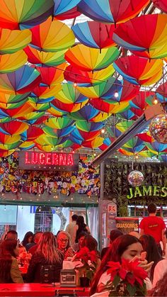 many colorful umbrellas are hanging from the ceiling above a crowded restaurant dining area with people sitting at tables