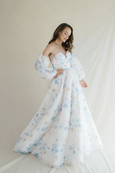 a woman wearing a white and blue floral print dress with long sleeves, standing in front of a white backdrop