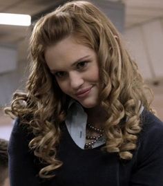 a woman with long curly hair smiling and looking at the camera while standing in an office