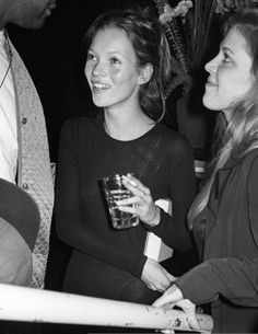 black and white photograph of three women smiling at each other with drinks in their hands