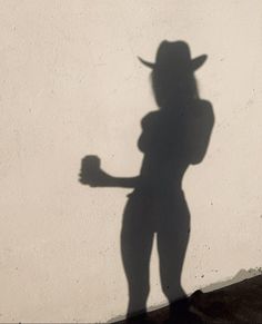 the shadow of a person wearing a cowboy hat and holding a baseball bat in their hand