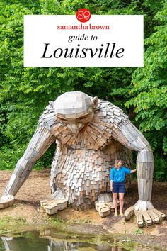 a woman standing next to a large wooden sculpture in front of some trees and water