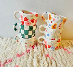 four coffee cups with designs on them sitting on a blanket in front of a white wall