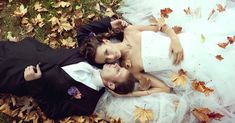 a bride and groom laying on the ground in autumn leaves