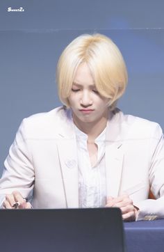 a person sitting at a table with a laptop in front of them and wearing a white jacket