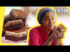 a woman holding up a piece of cake next to a pile of brownies on a table