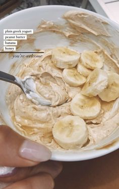 a person holding a spoon in a bowl of peanut butter and banana slices on top