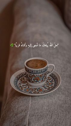 a cup of coffee sitting on top of a saucer next to a couch with arabic writing