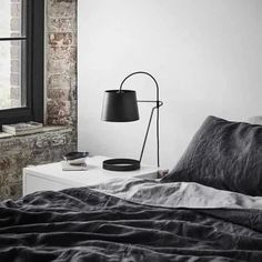 a bed with a black lamp on top of it next to a window and a brick wall