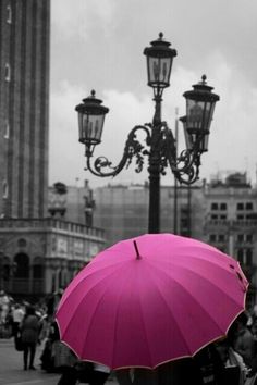 people are standing under pink umbrellas in front of street lamps on a cloudy day