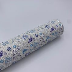 a roll of silver and blue glitter paper with snowflakes on the side, sitting on a white surface