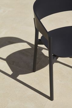 a black chair sitting on top of a cement floor next to a shadow cast by the sun