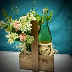 a bottle of wine and some flowers in a wooden box on a table with a blue background