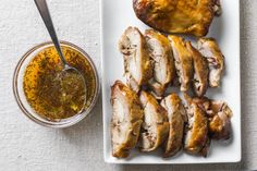 sliced chicken on a white plate next to a bowl of mustard