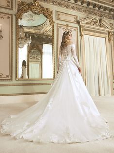 a woman in a white wedding dress standing next to a mirror and chandelier