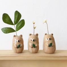 three ceramic bears with plants in their mouths on top of a wooden shelf next to a white wall