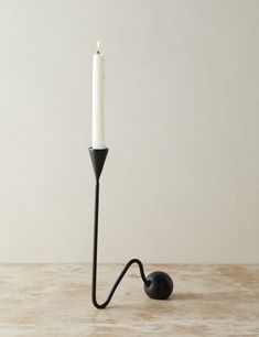 a black candle holder with a single white candle on it's end and a black hook in the middle