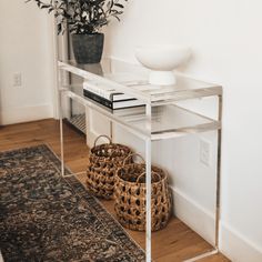 a white table with some baskets on top of it and a plant next to it