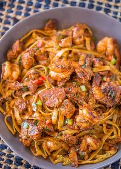 a bowl filled with pasta and meat on top of a blue table cloth next to a fork