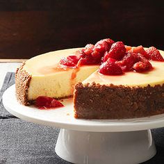 a cheesecake with strawberries is on a white cake plate and sits on a table