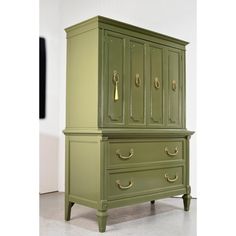 a green armoire with brass handles on it's sides and drawers in the middle