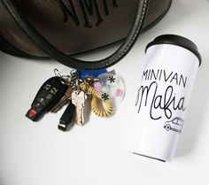 a coffee cup and keys are sitting next to a handbag on a white table