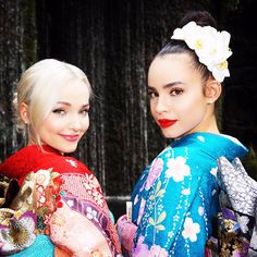 two beautiful women standing next to each other in kimonos with flowers on their hair