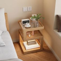 a small wooden table with some plants on it and an alarm clock next to the bed