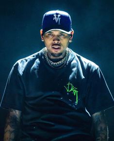 a man sitting in a chair wearing a blue hat and black t - shirt with green writing on it