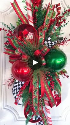 a christmas wreath hanging on the front door with ornaments and ribbons around it's edges