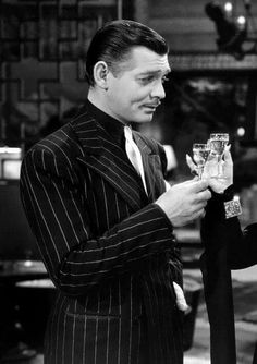 a man in a pinstripe suit holds a glass of wine while standing next to a woman