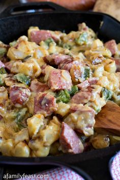 a skillet filled with ham and broccoli covered in cheese next to a wooden spoon