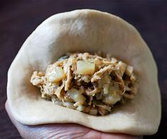 a person holding food in their hand with other foods on the table behind them, including an uncooked tortilla shell