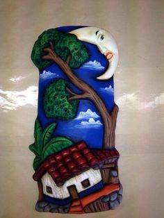 a ceramic wall hanging with a house and tree in the sky on it's side