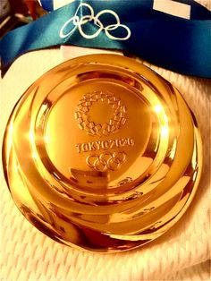 an olympic gold plate sitting on top of a white cloth next to a blue ribbon