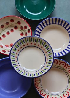 four plates are stacked on top of each other in different colors and designs, one has berries painted on it