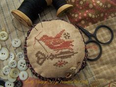 a pair of scissors and some thread on a table next to sewing needles, spools and buttons