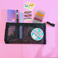 a black bag filled with lots of different items on top of a pink tablecloth