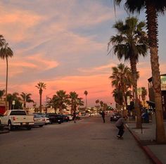 a skateboarder is riding down the street in front of palm trees at sunset