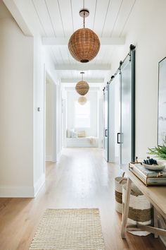 a long hallway with white walls and wooden flooring, two hanging lamps on the ceiling