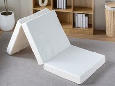 a white mattress sitting on top of a floor next to a book shelf and bookshelf