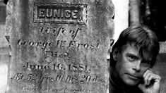 a black and white photo of a man leaning against a grave stone with the name of george frost on it