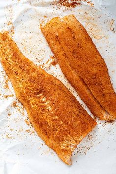 two fish fillets are sitting on top of some white paper with seasoning sprinkles