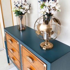 two vases with flowers sit on top of a blue dresser next to a mirror