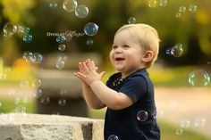 a little boy that is standing in front of soap bubbles and smiling at the camera