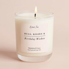 a candle that is sitting on a pink surface with the words hugs, kisses & birthday wishes printed on it