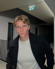 a young man in a white shirt and black jacket is posing for the camera with his hands in his pockets