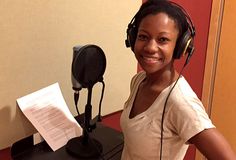 a woman standing in front of a microphone with headphones on and papers next to her