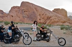 some people are sitting on their motorcycles in the middle of the desert and one person is standing next to them